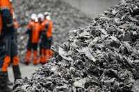 a group of workers in orange vests standing next to a pile of aluminium scrap