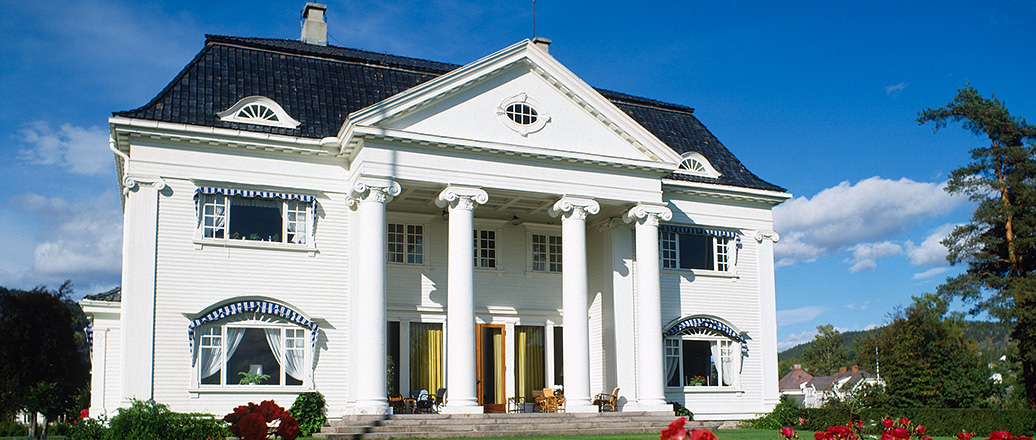 Hvitt herskapshus i rosehage.